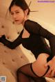 A woman in a black bodysuit and stockings sitting on a bed.