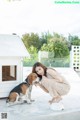 A woman kneeling down next to a dog in front of a dog house.