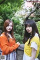 Two young women standing next to each other near a tree.