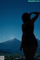 A woman standing in front of a mountain with her back to the camera.