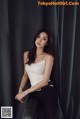 A woman in a white tank top and black pants posing for a picture.