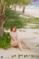 A woman in a bikini sitting under a palm tree on the beach.