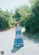 A woman in a blue dress and hat standing on a road.