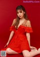 A woman in a red dress sitting on a red background.