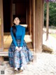 A woman in a blue turtle neck sweater and plaid skirt sitting on a porch.