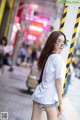 A young woman wearing glasses standing on a city street.