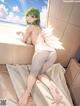 A woman with green hair and white wings sitting on a bed.