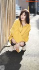 A woman in a yellow coat is sitting on the ground.